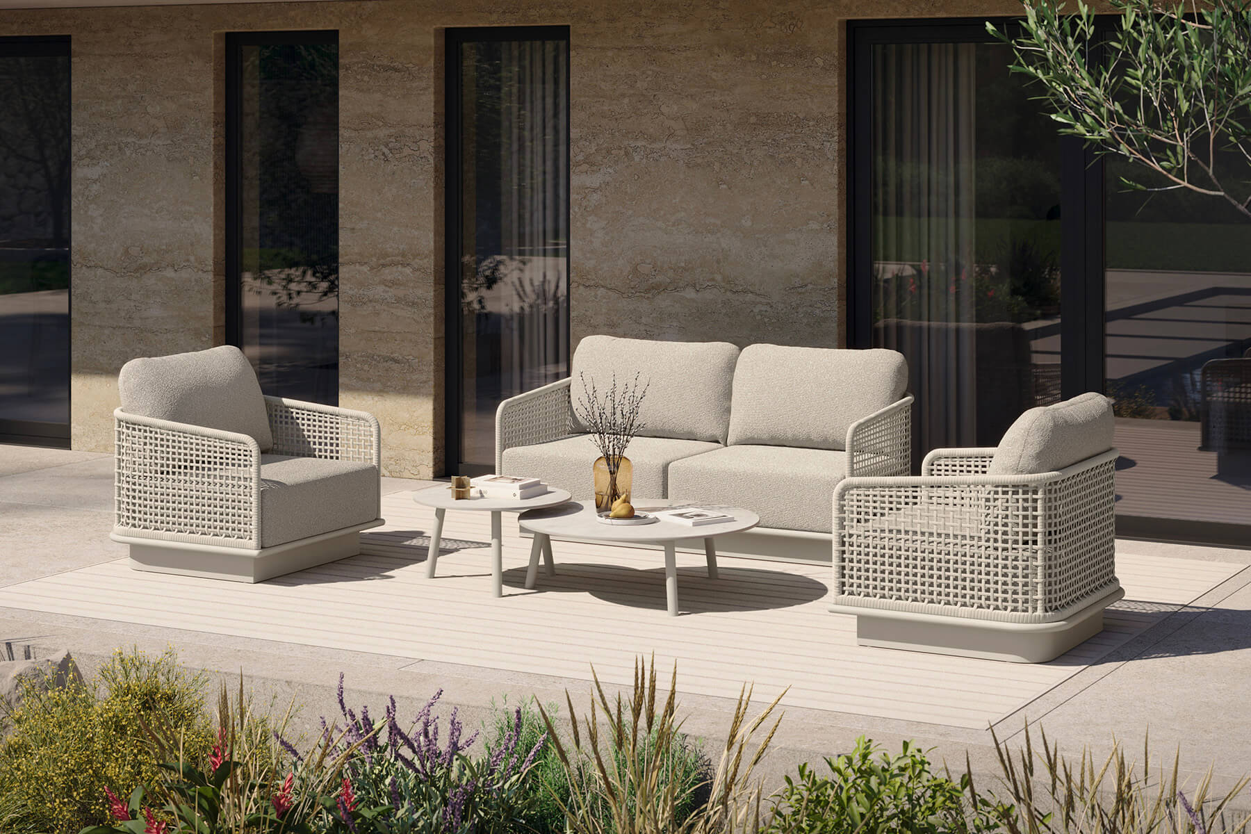 Lounge-Gruppe aus hellem Geflecht mit Zweisitzer, zwei Sesseln und zwei runden Beistelltischen auf einer Terrasse vor einer Natursteinfassade